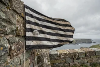 Drapeau breton Gwenn ha du accroché sur un mur en granit ancien face à la côte atlantique, mettant en valeur les neuf bandes noires et blanches et le motif hermine