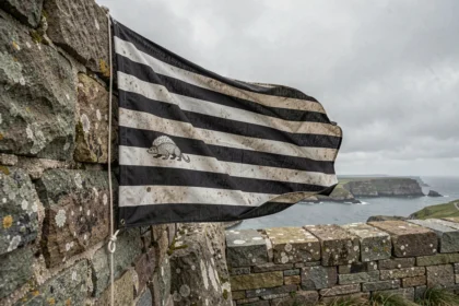 Drapeau breton Gwenn ha du accroché sur un mur en granit ancien face à la côte atlantique, mettant en valeur les neuf bandes noires et blanches et le motif hermine