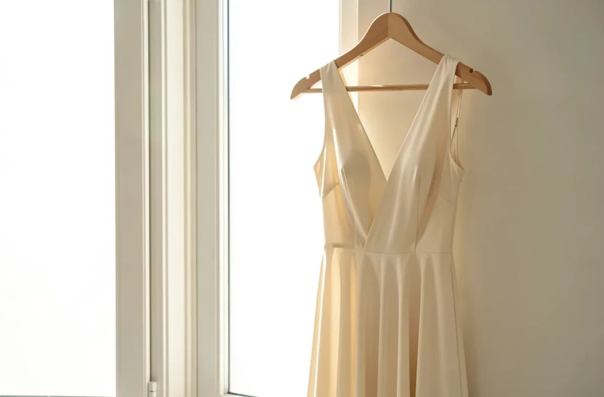 Robe claire et fond de robe couleur chair sur cintres devant une fenêtre